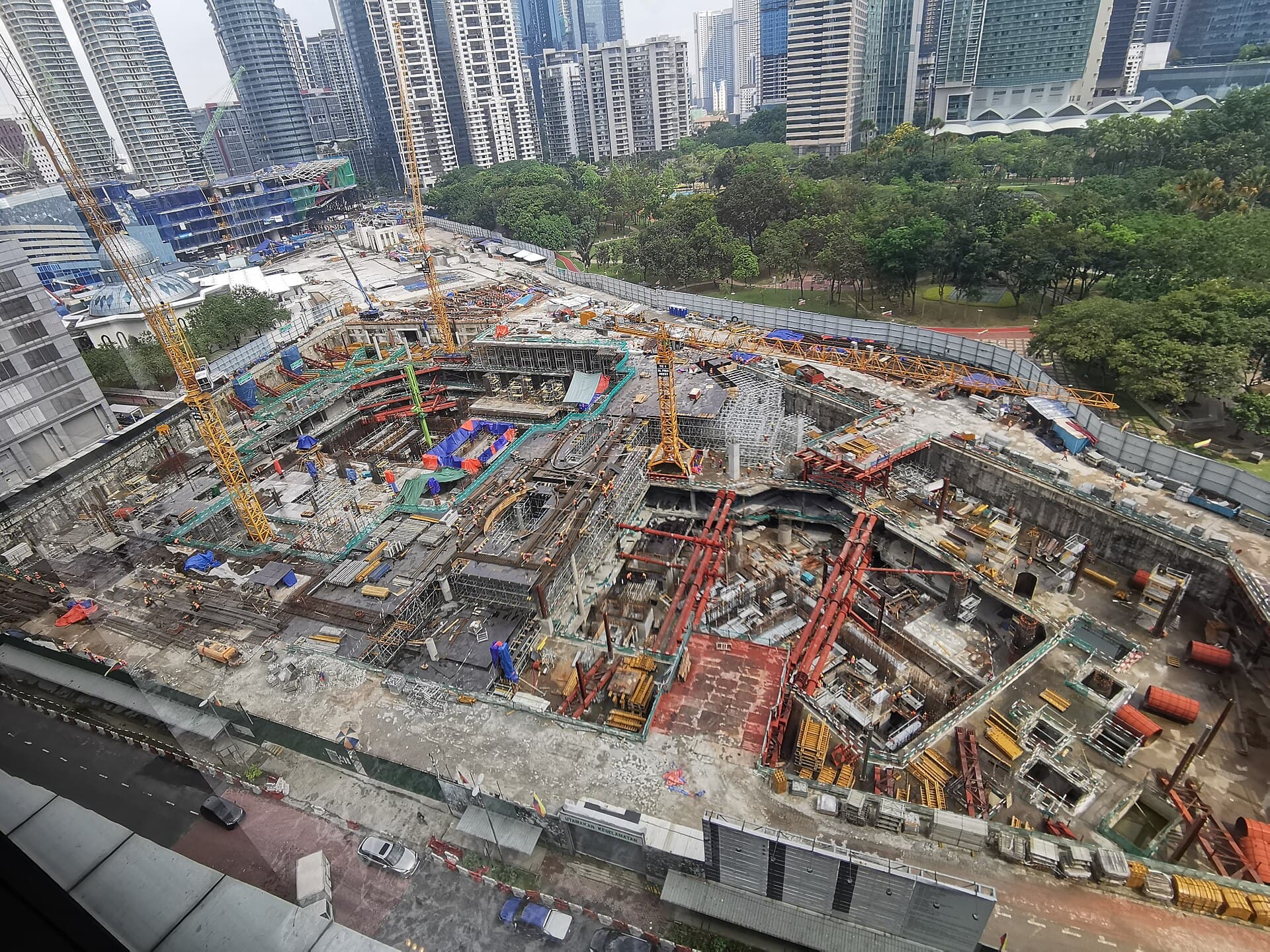 A large construction site in central Kuala Lumpur, with tower cranes over an excavated basement and high-rise towers behind it.